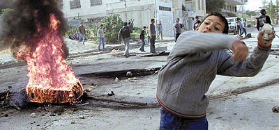A young Palestinian boy, standing next to a burning tyre, hurls stones towards an Israeli occupation army jeep during clashes in the West Bank city of Nablus on Tuesday (photo by Abed Omar Qusini/Reuters, Jordan Times, 1/29/03). 