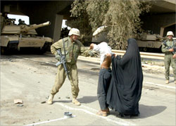 An elderly Iraqi man stopped by US soldiers before he is allowed to pass under a bridge in Baghdad. He had to lift up his clothes to show that he doesn't have explosives around his waist. (Alquds, 4/11/03).